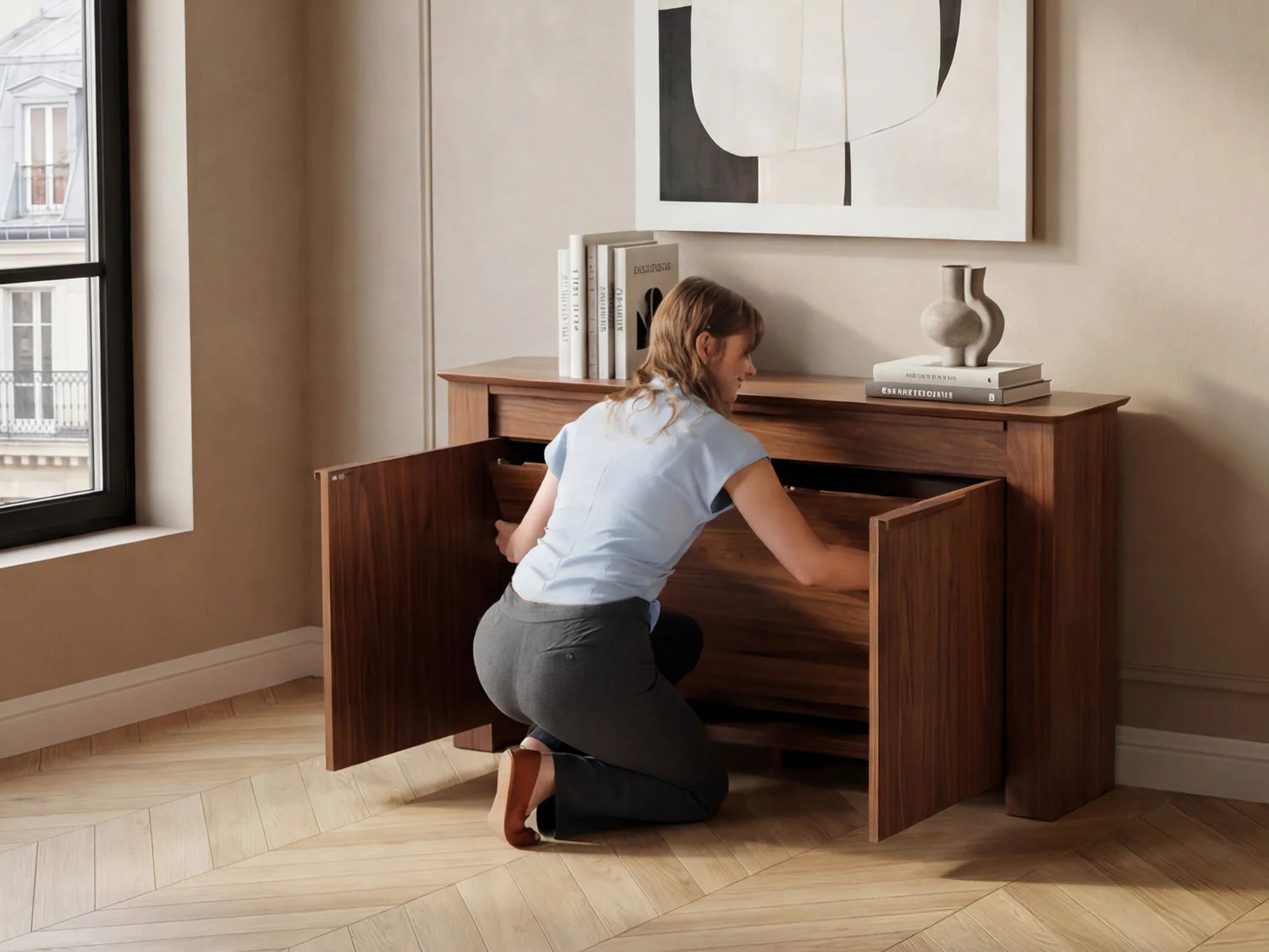 Person opening a wooden cabinet in a room with a window and decorative items.