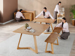 Four women assembling a wooden dining set in a room with a plant and rug.