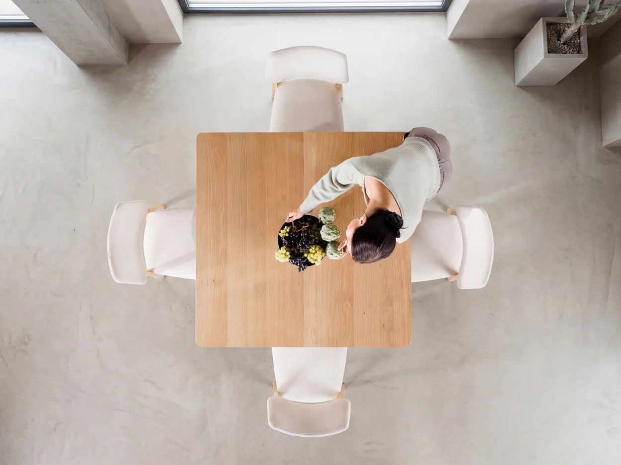 Person arranging flowers at a wooden table in a minimalistic room.