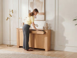 Woman opening a wooden desk in a room with light-colored walls and decor.