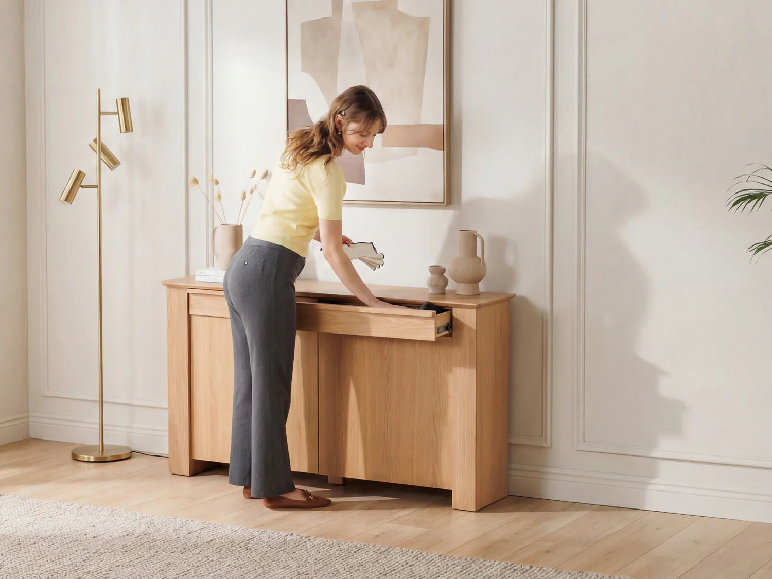 Woman opening a wooden desk in a room with light-colored walls and decor.