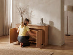 Woman assembling a wooden sideboard in a room with a lamp and vase.
