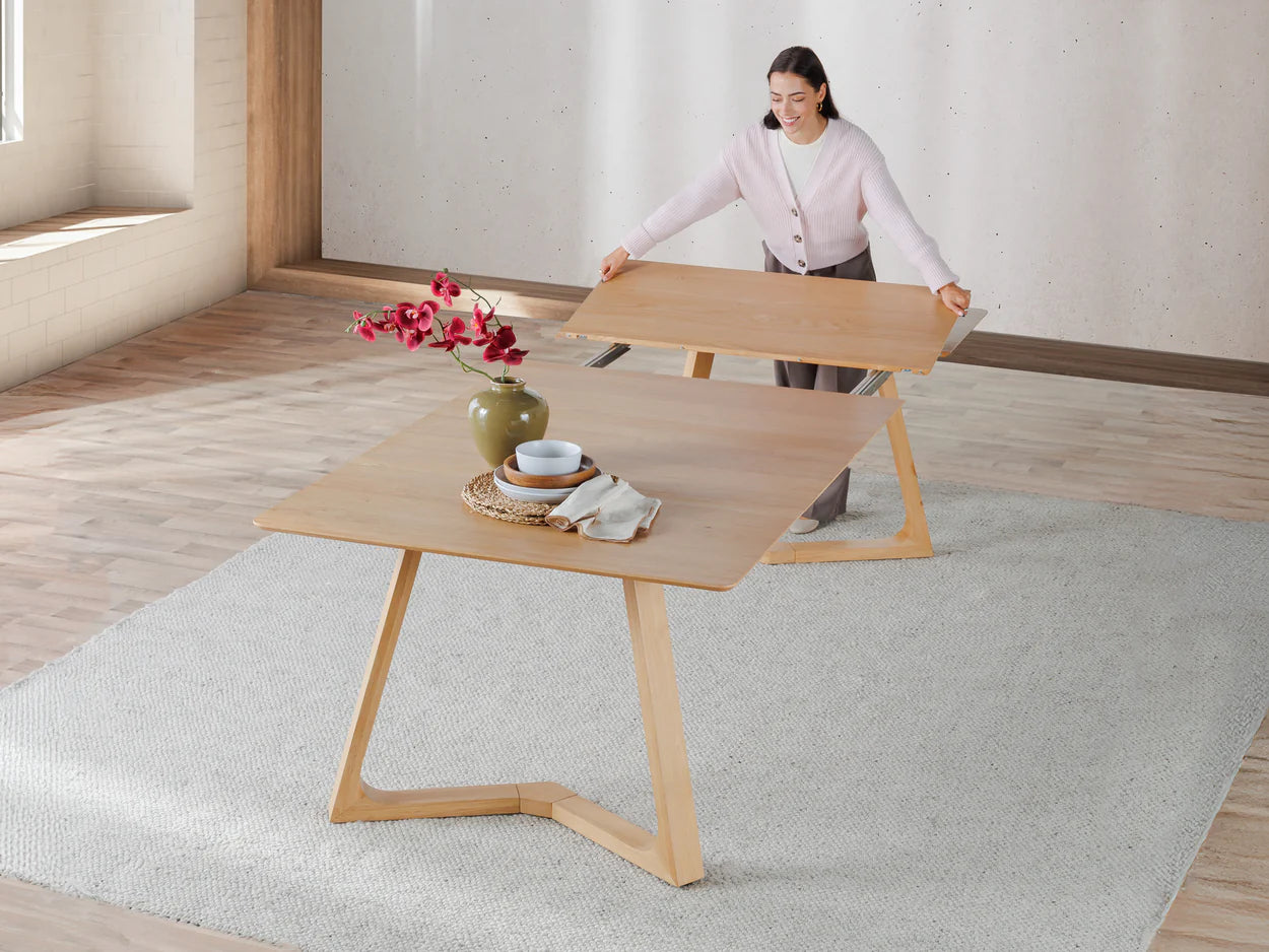 Woman arranging a wooden table in a minimalistic room with a rug and vase.
