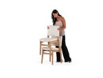 Woman holding a cushion next to two wooden stools with white cushions on a white background