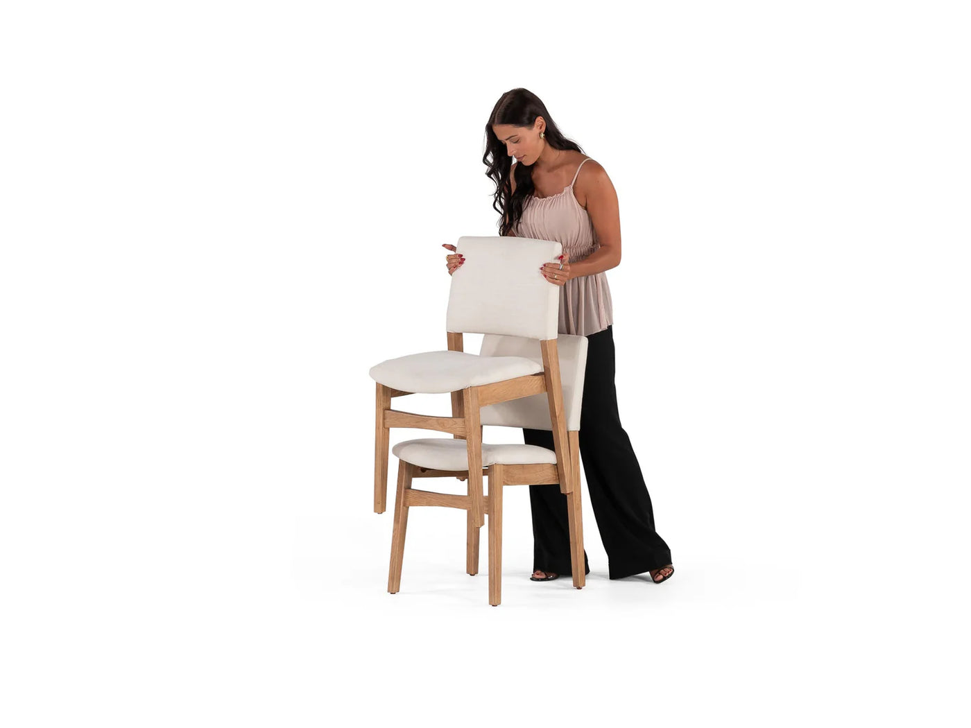 Woman holding a cushion next to two wooden stools with white cushions on a white background