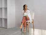 Woman sitting on a chair in a minimalistic room with white walls and a wooden floor.