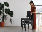 Woman in a red dress interacting with a black chair in a room with a large plant and window.
