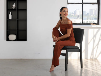 Woman in a rust-colored dress sitting on a black chair in a modern room with a cityscape view.