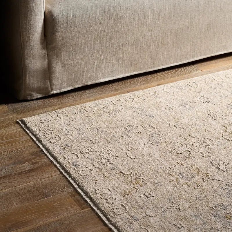 Beige rug on a wooden floor next to a beige sofa.