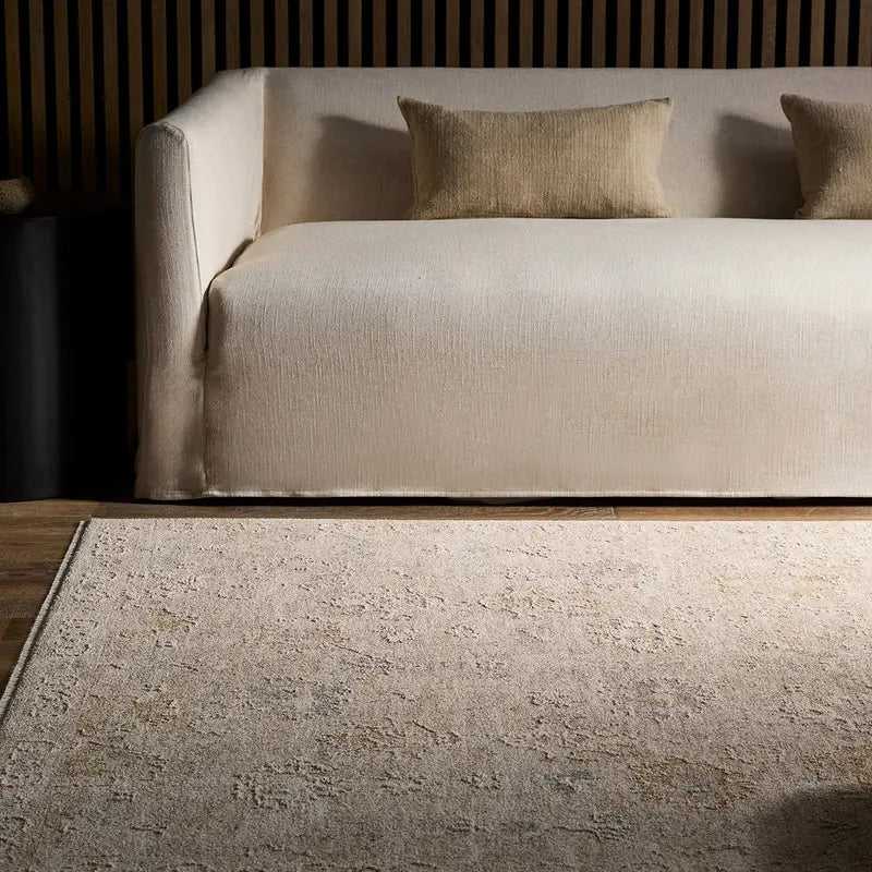 Beige rug in front of a beige sofa with brown cushions in a dimly lit room.