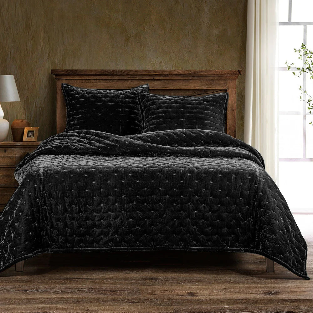 Dark quilted bedding set on a wooden bed in a bedroom setting.