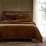 Brown quilted bedding set on a bed with a wooden headboard in a room with a window and plant.