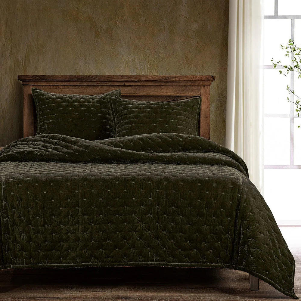 Dark green quilted coverlet on a bed with wooden headboard and pillows, against a textured wall.