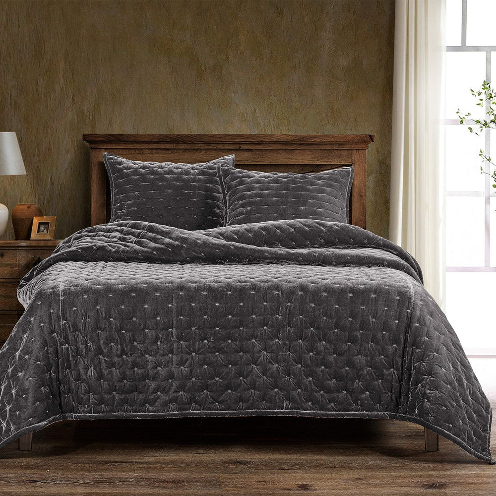 Gray quilted coverlet on a bed with wooden headboard and side tables in a room with a textured wall and window.