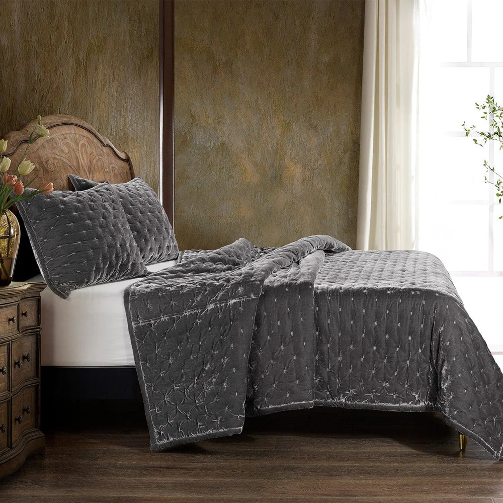 Gray quilted coverlet on a bed in a bedroom setting with a wooden headboard and side table.