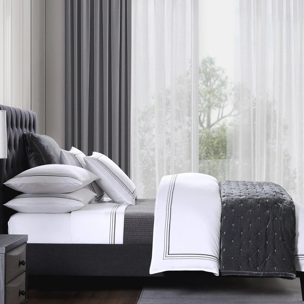 Bed with white bedding and gray quilt in a bedroom setting