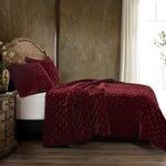 Bed with burgundy textured comforter and pillows in a bedroom setting.