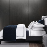 Bed with navy and white bedding against a dark paneled wall.