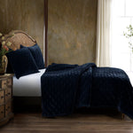 Navy blue textured blanket on a bed in a bedroom setting with a wooden headboard and side table.