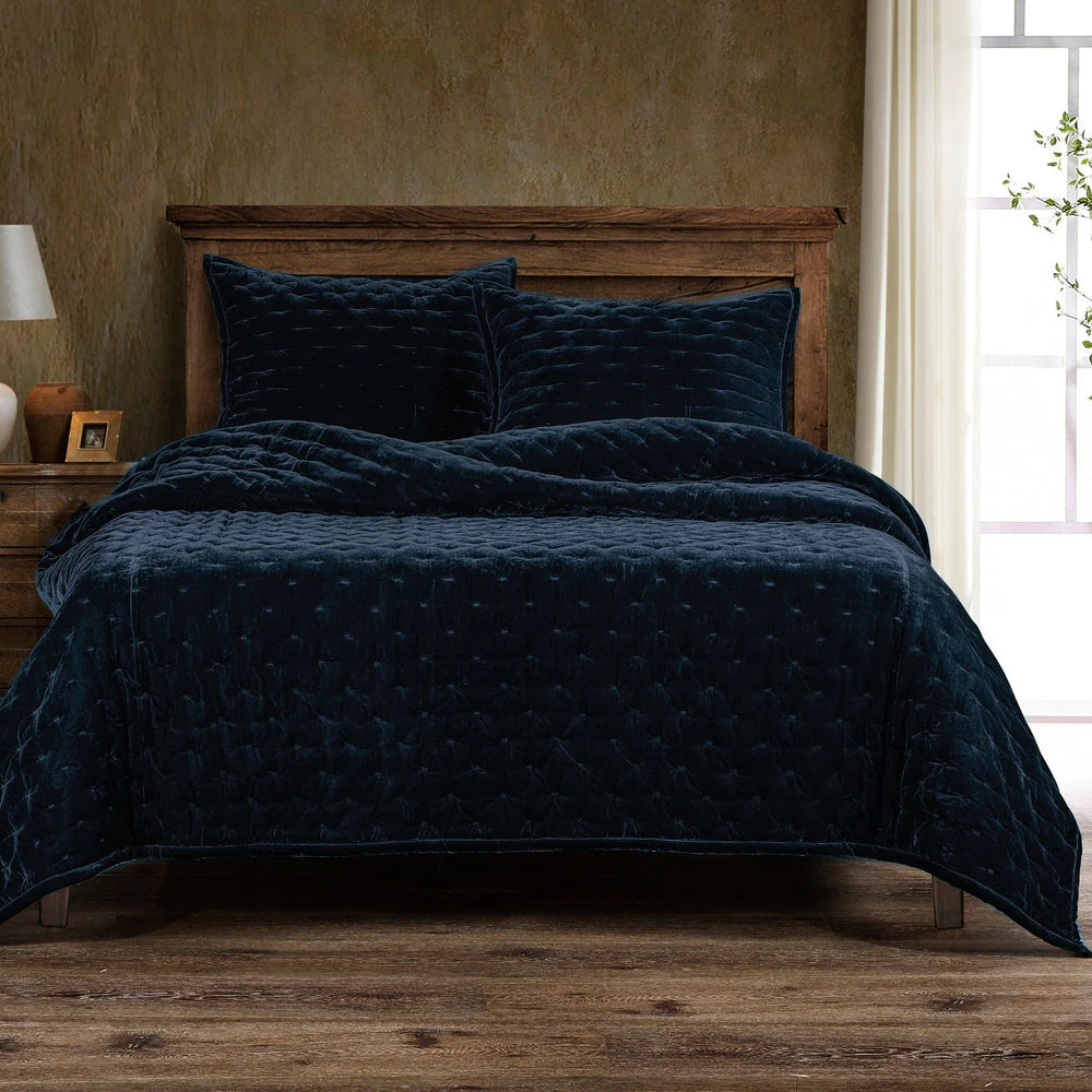 Navy quilt and pillows on a wooden bed in a bedroom setting.
