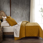 Bed with mustard yellow quilt and pillows in a bedroom setting.