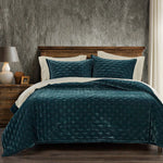 Teal quilted comforter on a bed with a wooden headboard and textured wall.