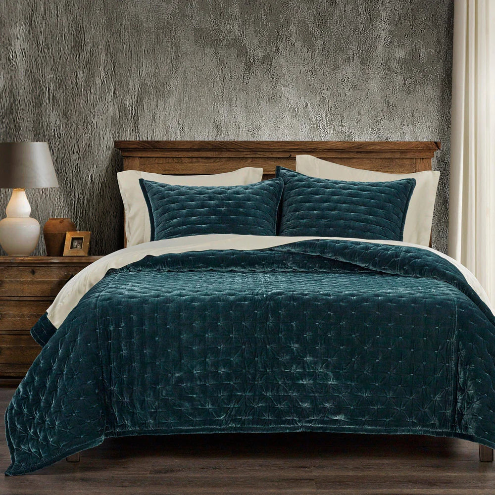 Teal quilted comforter on a bed with a wooden headboard and textured wall.