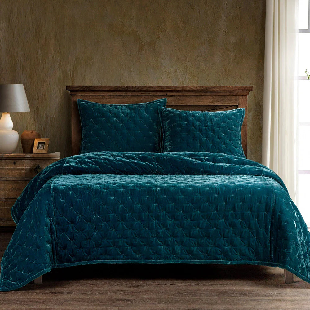 Teal quilt and pillows on a bed in a bedroom setting with a wooden headboard and lamp.