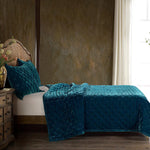 Teal textured bedspread and pillow on a bed in a bedroom setting.