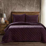 Bed with purple quilt and pillows against a textured wall.