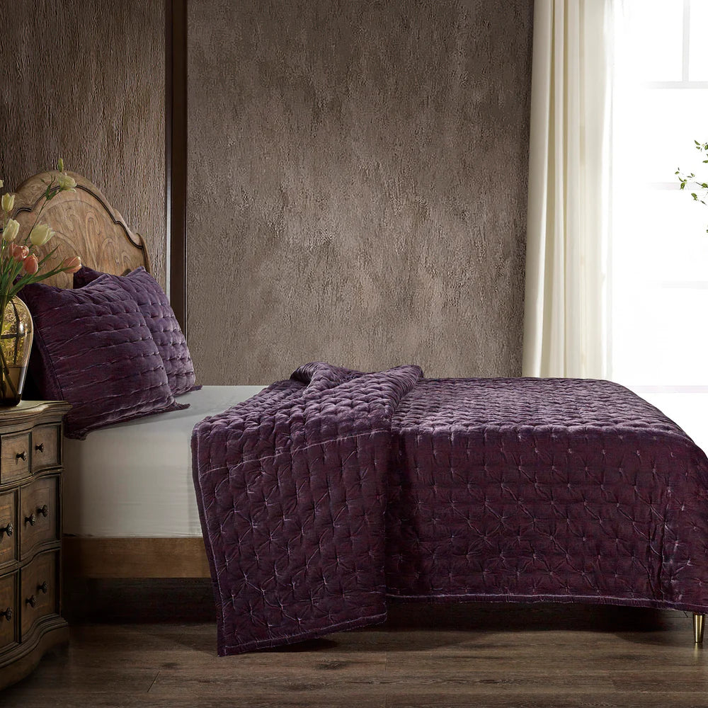 Bed with purple quilt and pillows in a bedroom setting