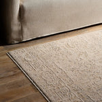 Beige textured rug on a wooden floor next to a beige sofa.