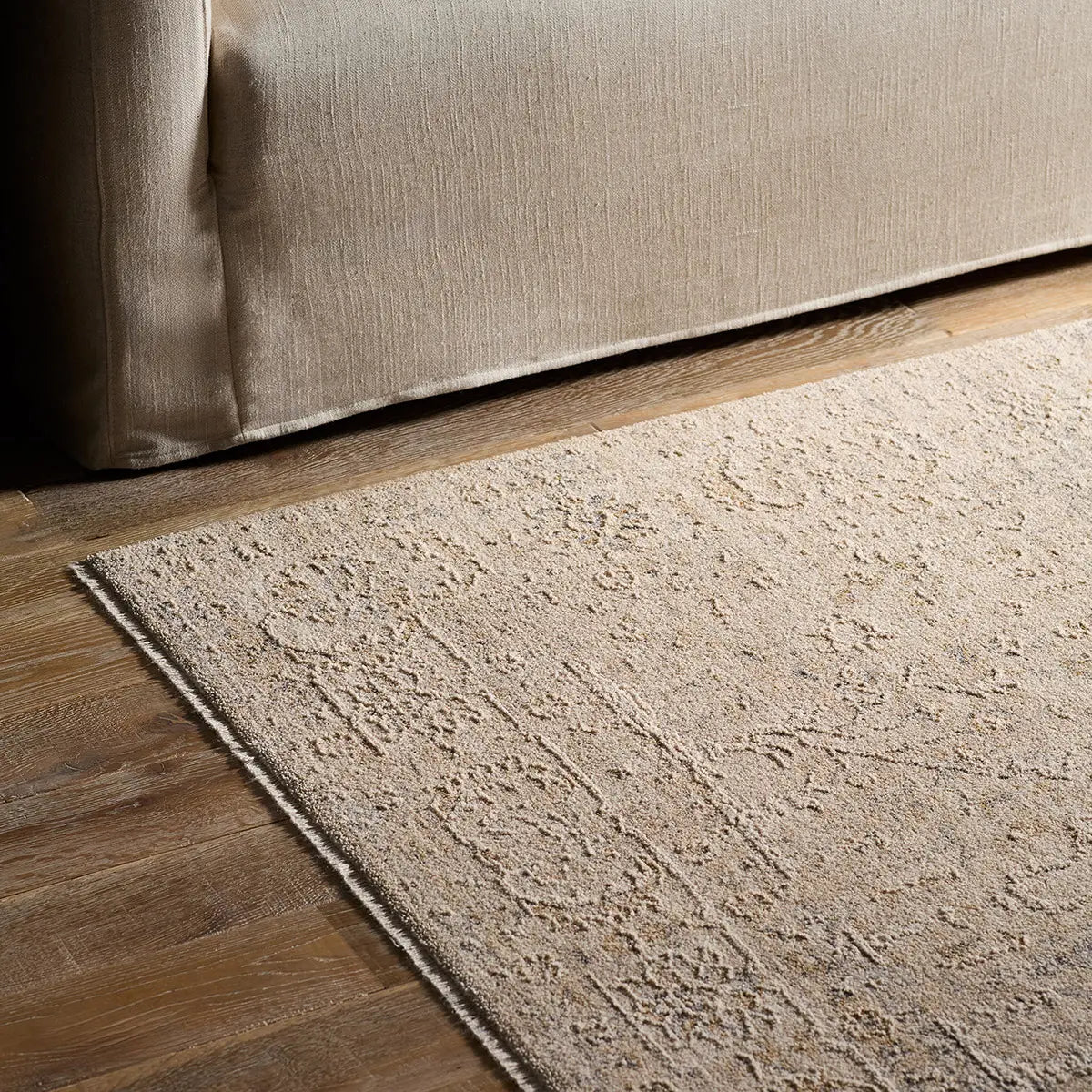 Beige textured rug on a wooden floor next to a beige sofa.