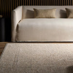 Beige sofa with textured cushions on a matching rug in a room with wooden flooring.