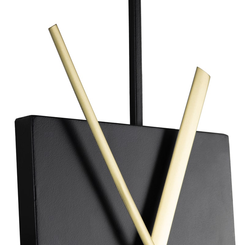 Close-up to a wall clock with a black circular frame and a central black square with gold-colored hands.