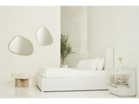 A modern bedroom scene with a low white bed, white nightstand, and two organic-shaped wall mirrors with thin gold frames on a light neutral wall.