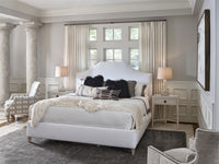 A white upholstered bed with a curved headboard in a bright, neutral-toned bedroom. The bed is dressed in white textured bedding with black and striped accent pillows, flanked by matching white nightstands with lamps.