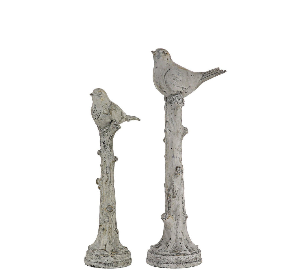 Two decorative bird statues on branches against a white background