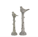 Two decorative bird statues on branches against a white background