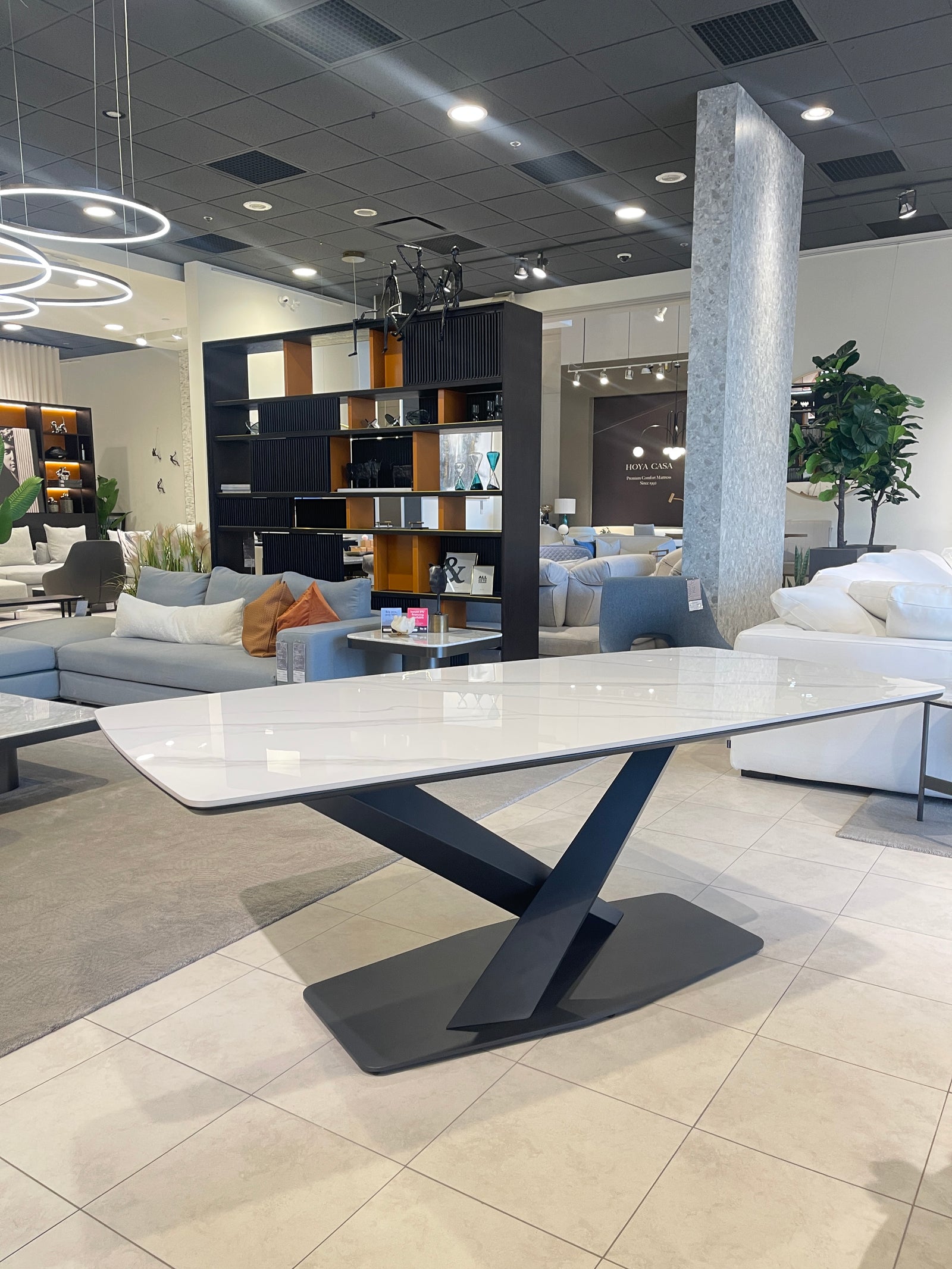 A modern dining table with a white marble pattern sinter stone top and a black metal X-shaped base, displayed in a showroom setting.