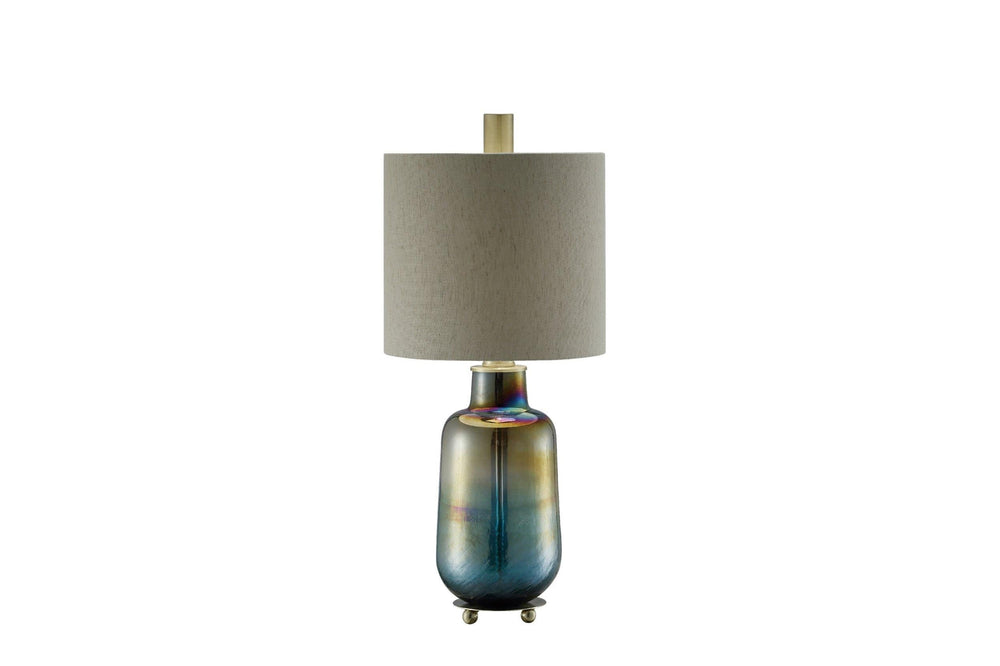 A tall table lamp with a teal iridescent glass base and a brass finish, topped with a beige shade.