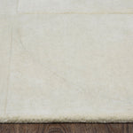 An ivory-colored wool area rug with a geometric patterned design, hand tufted with a cotton backing.