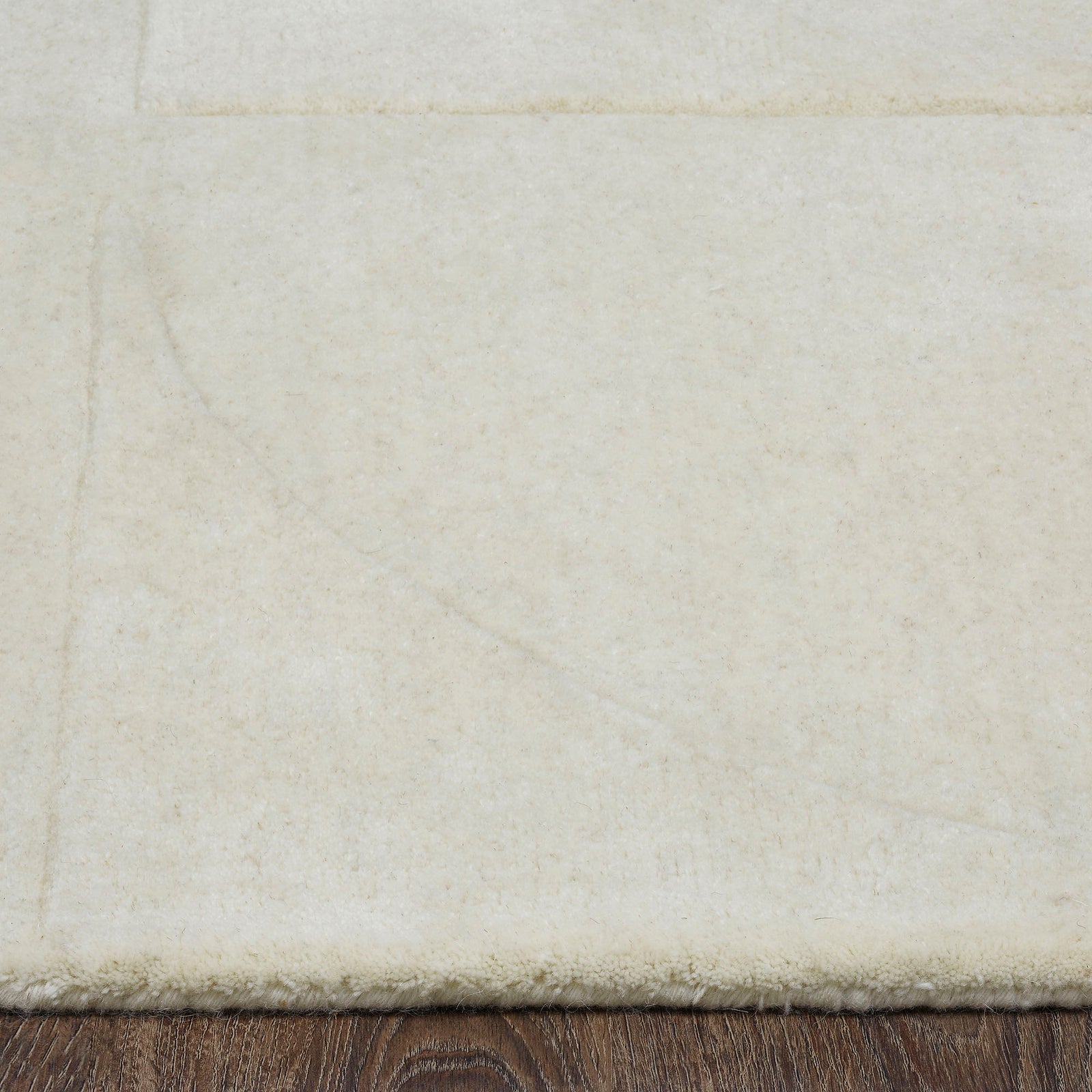 An ivory-colored wool area rug with a geometric patterned design, hand tufted with a cotton backing.