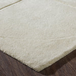An ivory-colored wool area rug with a geometric patterned design, hand tufted with a cotton backing.