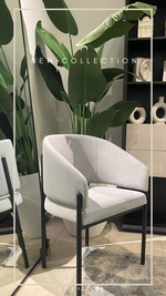 A modern white dining chair with a metal frame, displayed in a room with a plant and decorative items.