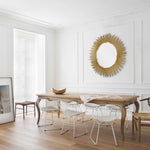 A round decorative mirror with a gold leaf finish frame designed to resemble a sunburst.