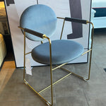 A contemporary brass dining chair with a blue seat and backrest, featuring a minimalistic design with subtle gold accents.