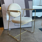 A contemporary brass dining chair with a white seat and backrest, featuring a minimalistic design with subtle gold accents.