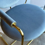 A contemporary brass dining chair with a blue seat and backrest, featuring a minimalistic design with subtle gold accents.