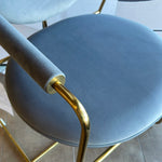 A contemporary brass dining chair with a blue seat and backrest, featuring a minimalistic design with subtle gold accents.